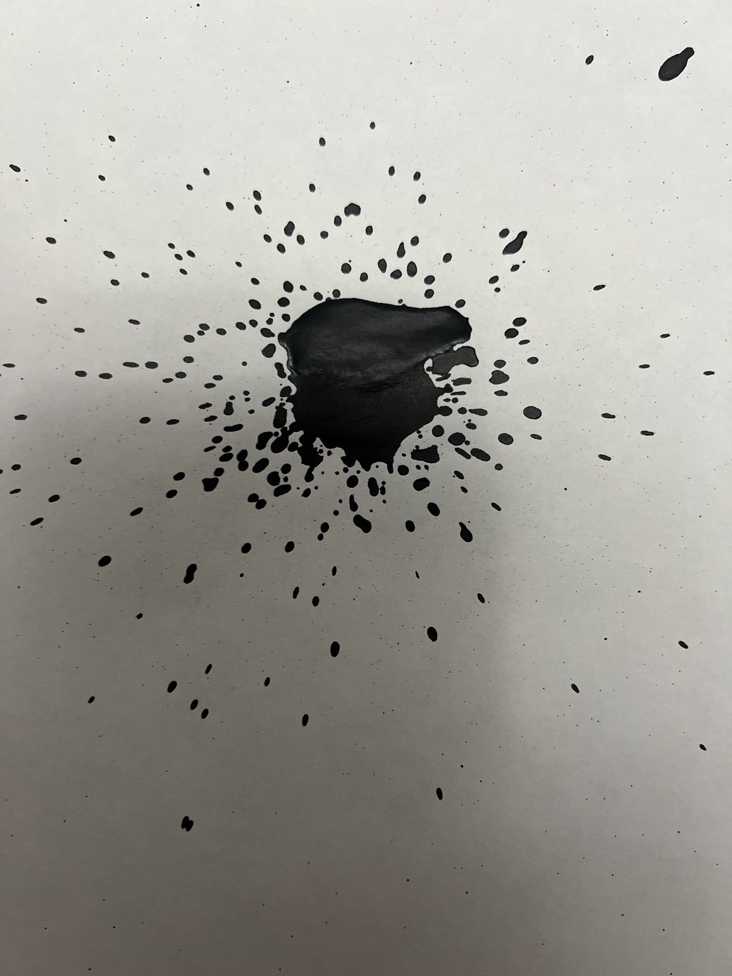 A pool of ink surrounded by splatter on white paper