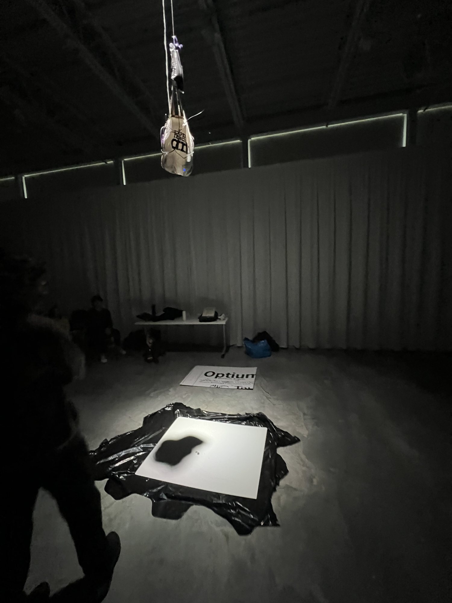 The dress rehearsal in a dark room: the ink bag hangs under a spotlight above a white board on the floor