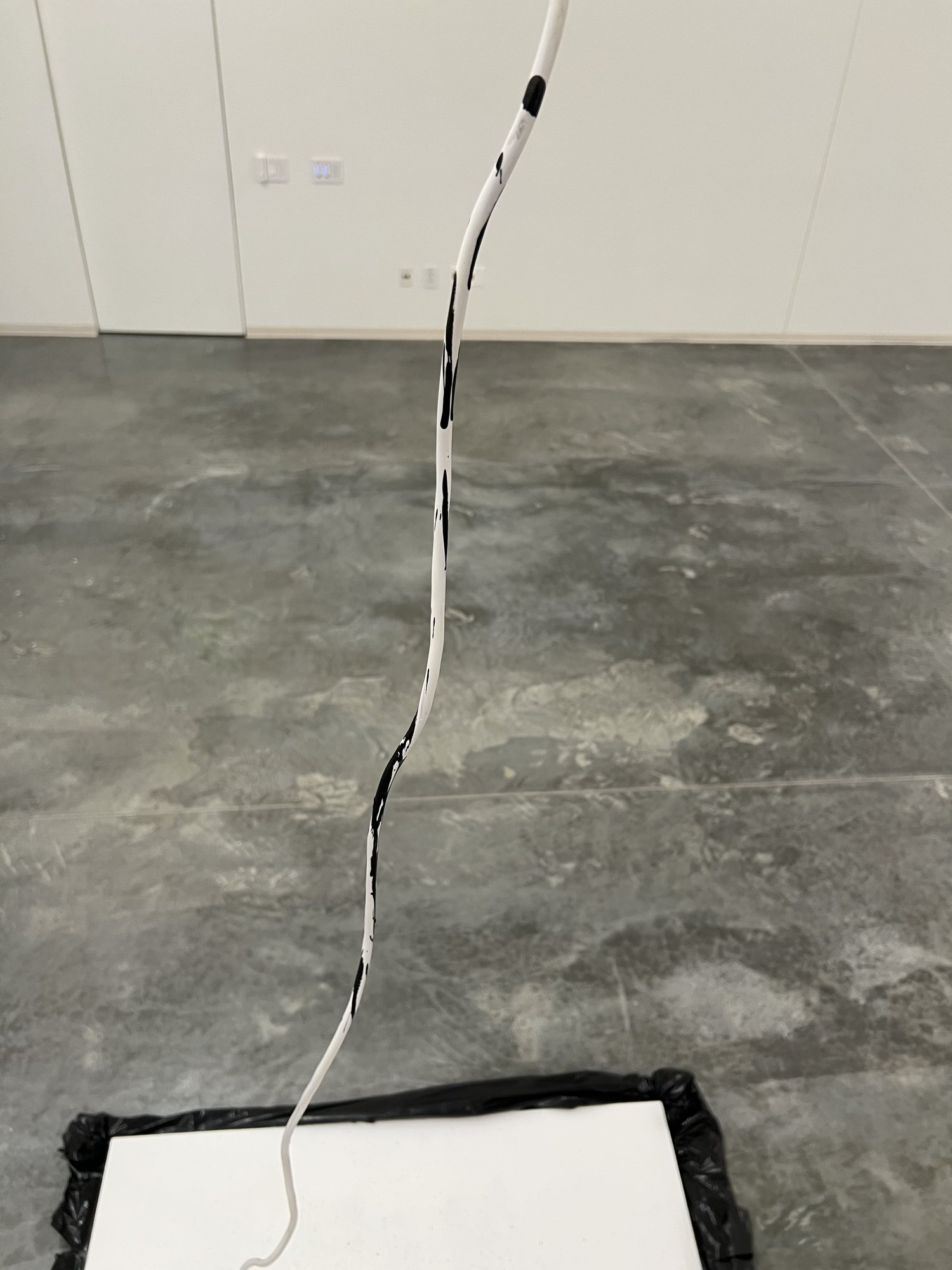 A white power cord hanging down to the canvas, marked with black ink where drops have hit it