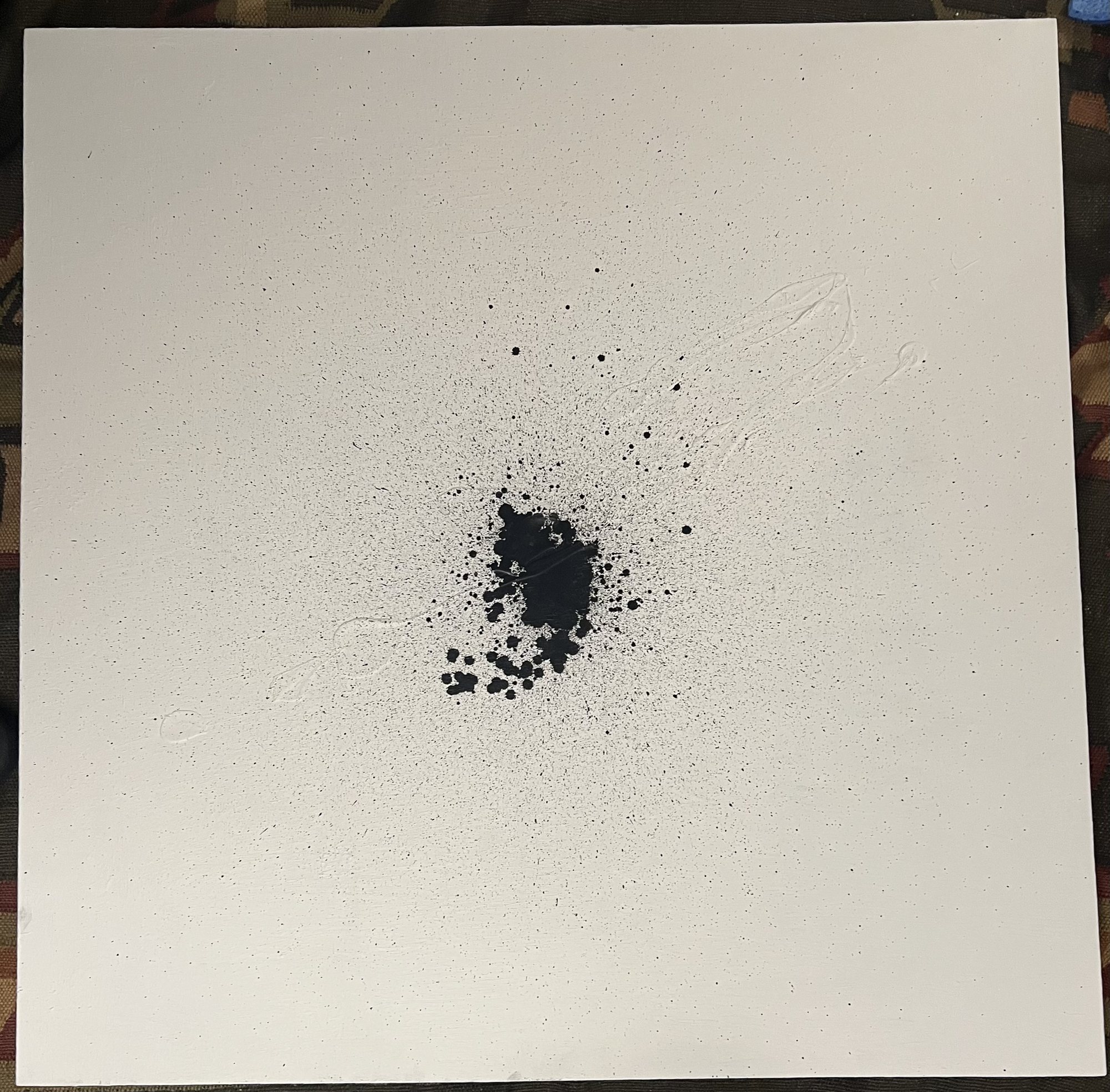 The finished canvas: a dense cluster of black ink at its center, surrounded by fine splatter